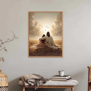 May include: A framed print depicts two figures embracing, seated in a field, with a bright light and birds in the sky. The artwork is in a wooden frame and hangs on a light gray wall. A decorative vase and bench are in the foreground.