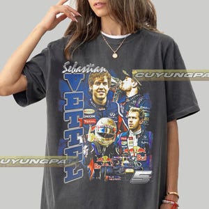 Puede incluir: Una camiseta de manga corta gris carbón con un estampado gráfico del piloto de Fórmula 1 Sebastian Vettel. El diseño incluye el nombre Sebastian Vettel en texto vertical azul, varias imágenes del piloto, un coche de carreras y el número 5.