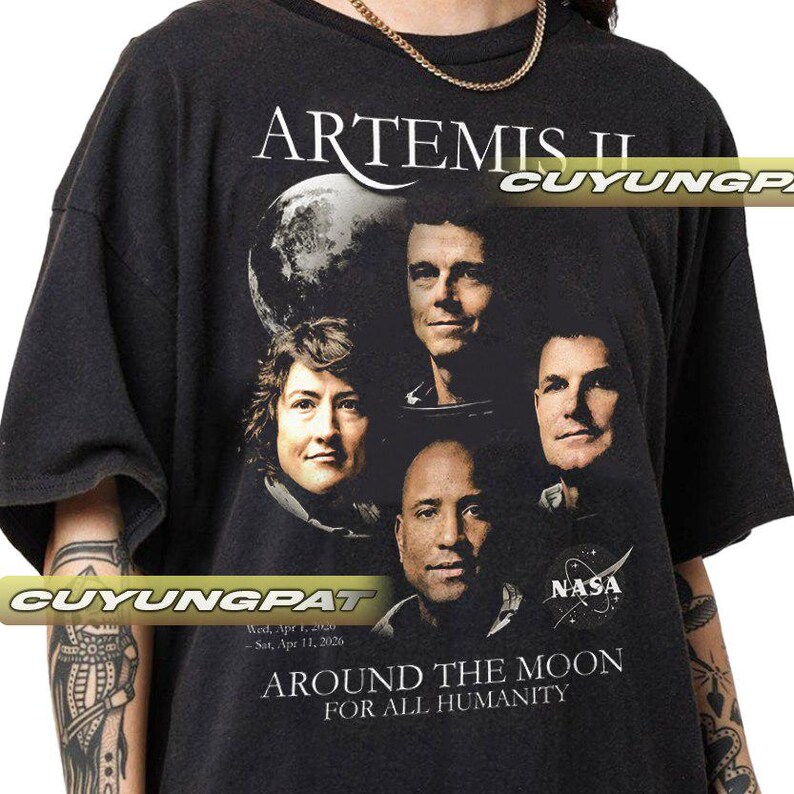 May include: Black t-shirt featuring the Artemis II mission. The shirt displays the mission name, a graphic of the moon, and portraits of four astronauts. Text on the shirt reads "AROUND THE MOON FOR ALL HUMANITY" and "NASA".