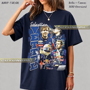 May include: A navy blue oversized t-shirt featuring a graphic print of Formula 1 driver Sebastian Vettel. The design includes the text "Sebastian VETTEL" and the number "5", along with multiple images of the driver in racing gear and a car.