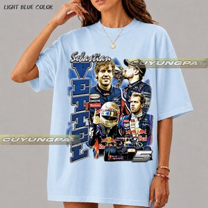 May include: A light blue t-shirt featuring a graphic print of Formula 1 driver Sebastian Vettel. The design includes multiple images of the driver, a racing helmet, a race car, the text "Sebastian Vettel," and the number "5" in a bold font.