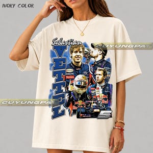 May include: An ivory-colored short-sleeve t-shirt featuring a graphic print of Formula 1 driver Sebastian Vettel. The design includes multiple images of the driver, a racing helmet, a race car, the text "Sebastian VETTEL", and the number 5.