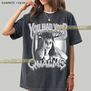May include: A graphite-colored short-sleeve t-shirt featuring a distressed white graphic print of a person with antlers on their head. The text "YOU HAD YOUR QUALMS" is printed in a stylized, jagged font above and below the central illustration.