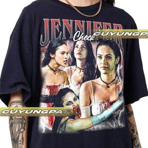 K&ouml;nnte beinhalten: Schwarzes T-Shirt mit einer Grafik einer Frau und dem Text "JENNIFER Check". Die Grafik enth&auml;lt mehrere Bilder der Frau mit einem Horror-Thema. Das Shirt hat kurze &Auml;rmel und einen Rundhalsausschnitt.