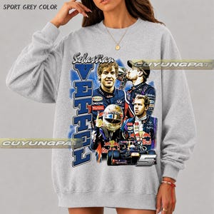 May include: A sport grey crewneck sweatshirt featuring a graphic print of Formula One driver Sebastian Vettel. The design includes multiple images of the driver in racing gear, a race car, the name Vettel in large blue letters, and the number 5.