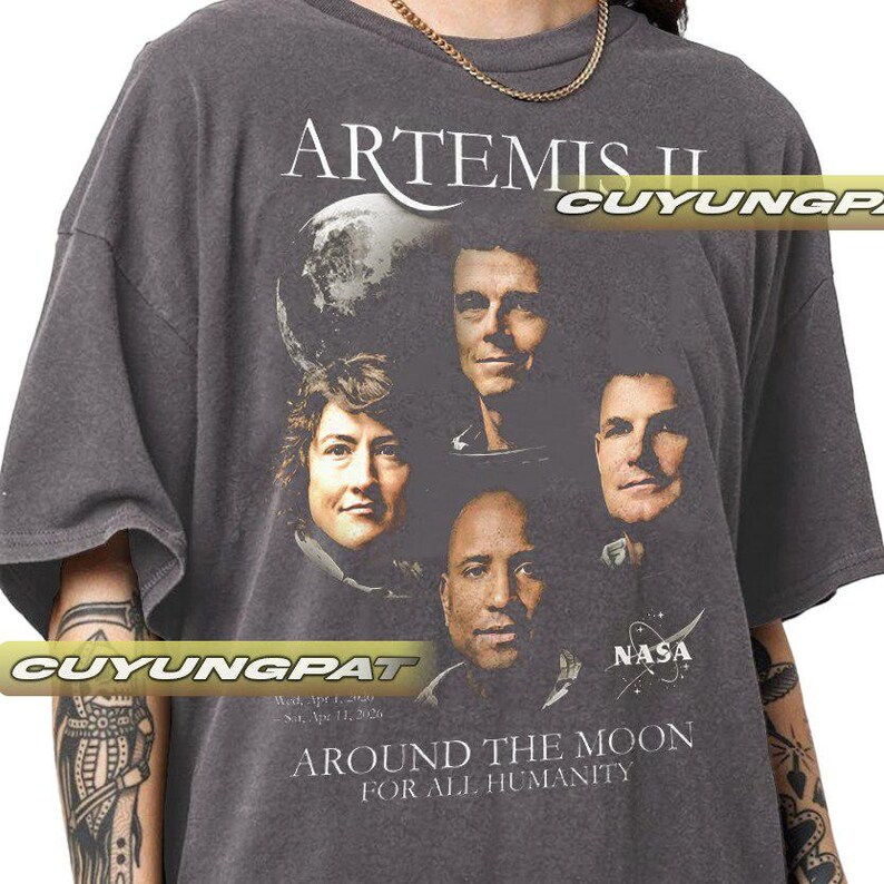 May include: Dark gray t-shirt featuring the text "ARTEMIS II" and a graphic of four astronauts and a planet. The shirt also includes the text "AROUND THE MOON FOR ALL HUMANITY" and the NASA logo.
