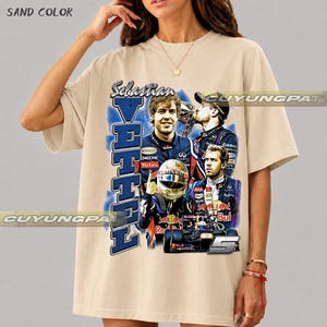 May include: A sand-colored short-sleeve t-shirt featuring a graphic print of Formula 1 driver Sebastian Vettel. The design includes multiple images of the driver, a racing helmet, a race car, the text "Sebastian VETTEL", and the number 5.
