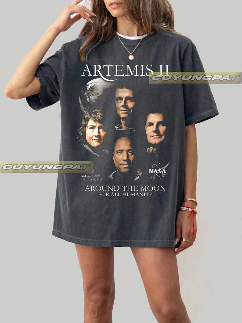 May include: Dark gray t-shirt featuring the text "ARTEMIS II" above a graphic of four astronauts and a planet. Below the image are the words "AROUND THE MOON FOR ALL HUMANITY" and the NASA logo.