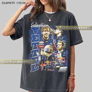 May include: A graphite-colored short-sleeve t-shirt featuring a graphic print of Formula 1 driver Sebastian Vettel. The design includes multiple images of the driver, a racing helmet, a race car, the text Sebastian Vettel, and the number 5.