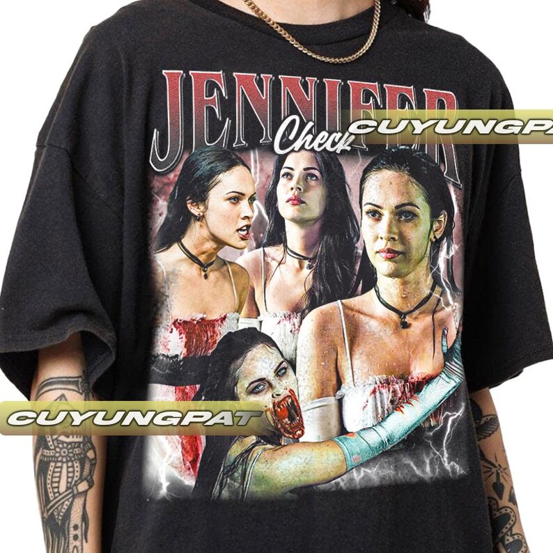 K&ouml;nnte beinhalten: Schwarzes T-Shirt mit einer Grafik einer Frau mit langen dunklen Haaren und dem Text "JENNIFER Check" in Rot und Wei&szlig;. Die Grafik hat einen Vintage-Look mit Blitz und einem Horror-Thema.