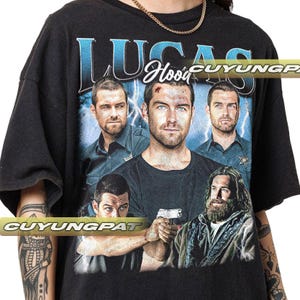 May include: Black t-shirt with a vintage-style graphic print featuring four men. The print includes the text "Lucas Hood" and "CUYUNGPAT".