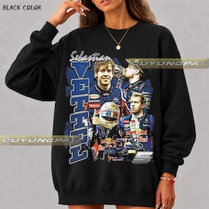May include: A black crewneck sweatshirt featuring a graphic print of Formula 1 driver Sebastian Vettel. The design includes multiple images of the driver in racing gear, a racing helmet, a race car, the text "Sebastian VETTEL", and the number 5.