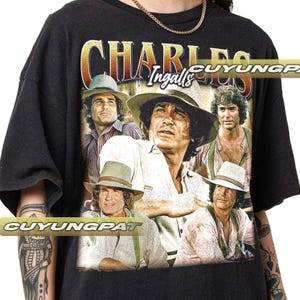 Peut inclure: T-shirt noir avec un graphique vintage de Charles Ingalls de la série télévisée "La Petite Maison dans la Prairie". Le graphique présente quatre images de Charles Ingalls, chacune avec une expression différente. Le texte "Charles Ingalls" est imprimé en lettres blanches au-dessus du graphique.