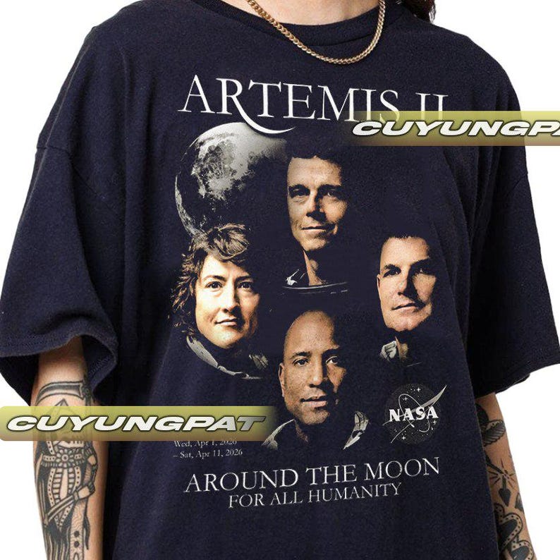 May include: Navy blue t-shirt featuring the text "ARTEMIS II" and the NASA logo. The shirt displays images of four astronauts and the text "AROUND THE MOON FOR ALL HUMANITY". The shirt also has the dates "Wed, Apr 1, 2026 - Sat, Apr 11, 2026".