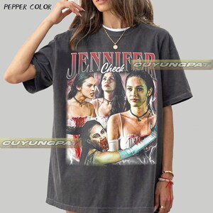 K&ouml;nnte beinhalten: Dunkelgraues T-Shirt mit einer Grafik einer Frau und dem Text "JENNIFER Check". Die Grafik enth&auml;lt mehrere Bilder der Frau. Das T-Shirt hat einen Vintage-Look.