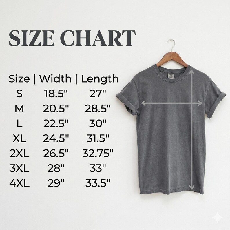 K&ouml;nnte beinhalten: Ein anthrazitfarbenes T-Shirt an einem Holzkleiderb&uuml;gel neben einer Gr&ouml;&szlig;entabelle. Die Tabelle listet die Gr&ouml;&szlig;en S bis 4XL mit den entsprechenden Breiten- und L&auml;ngenma&szlig;en in Zoll auf, von 18,5 mal 27 Zoll bis hin zu 29 mal 33,5 Zoll.