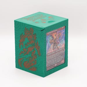 May include: A green card storage box with a hinged lid. The box features a detailed embossed design in a darker green color. A card is visible in the front, showcasing a fantasy illustration. The text "Dungeons & Dragons" is visible on the top of the box.