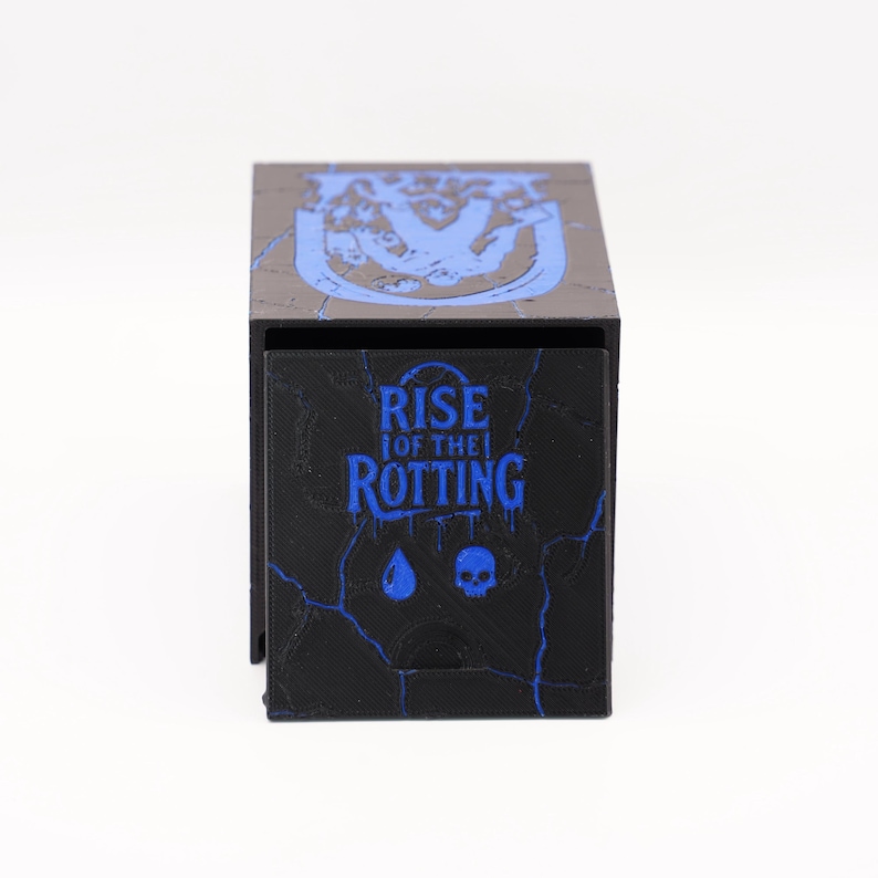 May include: Black and blue box with the text "RISE OF THE ROTTING" and a skull graphic. The box has a textured surface and a blue cracked design. The top of the box has a blue graphic design.