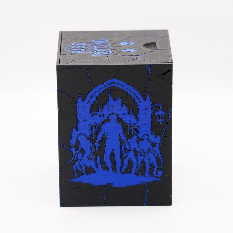 May include: Black cube-shaped box with a blue graphic design. The design features a silhouette of a figure in front of a building, with other figures around it. The top of the box has the text "RISE OF THE PUTTING".