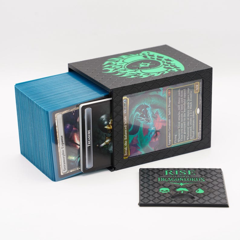 May include: Black card storage box with a green dragon design on the top and a window to display a card. A stack of blue cards is visible, along with a small black card with the text "RISE DRAGONLORDS".