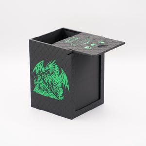 May include: Black box with a hinged lid, featuring a green dragon graphic on the side. The lid is slightly open, revealing the interior. The box has a textured, scale-like pattern. The text "RISE" is visible on the lid.