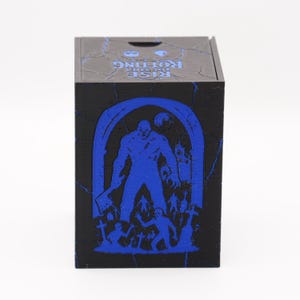 May include: Black wooden box with a blue graphic of a monster, figures, and tombstones. The box has the text "RISE OF THE ROTTING" in blue on the top. The box is square and has a hinged lid.