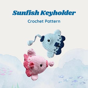 May include: A Sunfish Keyholder Crochet Pattern featuring two handmade crocheted fish, one light blue and one light pink, each with a small black eye and a dangling key ring attachment. The text Sunfish Keyholder Crochet Pattern is displayed.