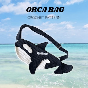 Puede incluir: Un bolso de ganchillo en blanco y negro con forma de orca, que incluye aleta dorsal, aletas laterales y cola. El bolso cuenta con una correa negra ajustable con herrajes metálicos. El texto ORCA BAG CROCHET PATTERN aparece sobre el bolso.
