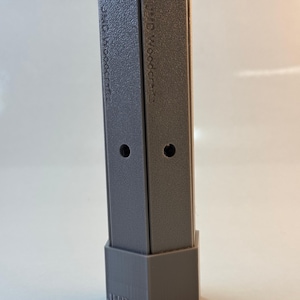 May include: A grey rectangular object with a textured surface and the text "JMD Woodcrafts" printed on the side. The object has a top and bottom cap and two small holes. The object is made of plastic.