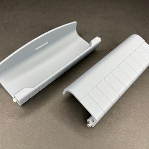 May include: Two gray plastic pieces with a ribbed texture. One piece is a curved, hollow tube, and the other is a flat, rectangular piece with a curved edge.