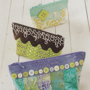 May include: Three colorful, handmade zippered pouches. The top pouch is light blue with a yellow floral pattern and a large green button. The middle pouch is green with white polka dots and a brown wavy trim. The bottom pouch is blue with green and purple patterns and white buttons.
