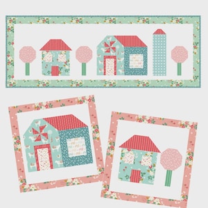 May include: A quilt pattern with the text "Homestead Runner and Pillow Pattern." The design features a runner and two pillow patterns with houses, trees, and a floral border. The pillow size is 24" x 24", and the runner size is 26" x 70".