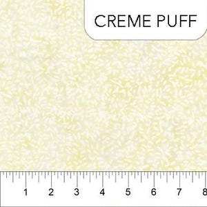 Pode incluir: Tecido creme claro com um padrão sutil e texturizado. O tecido tem um tom amarelo claro e um design repetitivo de pequenas formas semelhantes a folhas. A palavra "CREME PUFF" está impressa em preto sobre um fundo branco. Uma régua está na parte inferior.