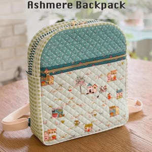 May include: The Ashmere Backpack features a quilted design with a light green and white gingham side panel. The front displays a light green fabric with a small house and tree print, a teal polka dot top section, and a gold zipper closure.