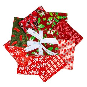 May include: A stack of folded fabric squares tied with a white ribbon featuring the text "Emma's Colorfully". The fabric patterns include red and green Christmas stockings, white snowflakes, bows, geometric lines, and floral motifs in red and green.