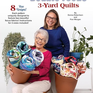Peut inclure: Deux femmes tiennent des courtepointes roulées dans des pots en terre cuite. Les courtepointes sont de couleurs et de motifs variés. Le texte sur l'image indique "Double Focus 3-Yard Quilts" et "8 New Designs! Each pattern uniquely designed to feature two beautiful focus fabrics! Instructions for 3 sizes included!"  Par Donna Robertson et Fran Morgan.