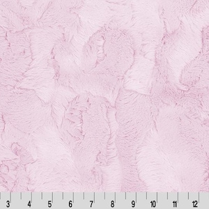 May include: A close-up of a light pink fabric with a textured, plush surface. The fabric has a swirling pattern and a soft, fuzzy appearance. A ruler is at the bottom of the image, with measurements in inches.