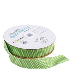 May include: A spool of green and white gingham single-fold quilt binding tape. The label reads "Single-Fold Quilt Binding" and "Gingham". The tape is 2.5 inches wide and made of 100% cotton.