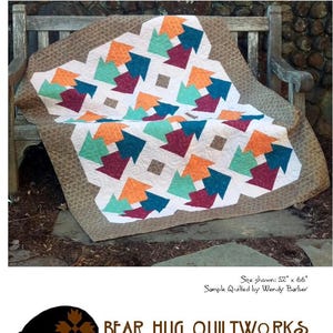 May include: A handmade quilt with a geometric arrow pattern in teal, orange, and burgundy on a white background. The quilt, measuring 52" x 66", is displayed on a wooden bench. The word "THATAWAY" is at the top.