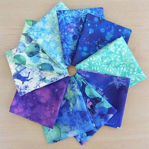 May include: A collection of fabric squares arranged in a circular pattern. The fabrics feature various shades of blue, teal, and purple with snowflake, floral, and abstract designs. A small, round, wooden piece is in the center of the arrangement.