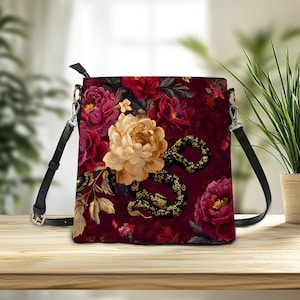 Peut inclure: Sac bandoulière carré avec un motif floral et serpent. Le sac présente un fond bordeaux avec de grandes fleurs colorées et un serpent noir avec des accents dorés. Le sac a une sangle noire et des accessoires argentés.