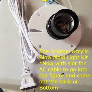 May include: White plastic light socket with a black electrical cord and a white plug. The socket has a slot for an AC cable to go into the figure and come out the back or bottom. The text "The Original Acrylic Blow Mold Light Kit *Now with slot for AC cable to go into the figure and come out the back or Bottom." is written below the socket.