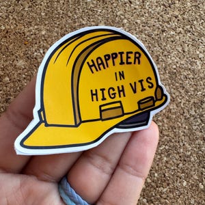 May include: A yellow construction worker hard hat sticker with the text "Happier in High Vis".