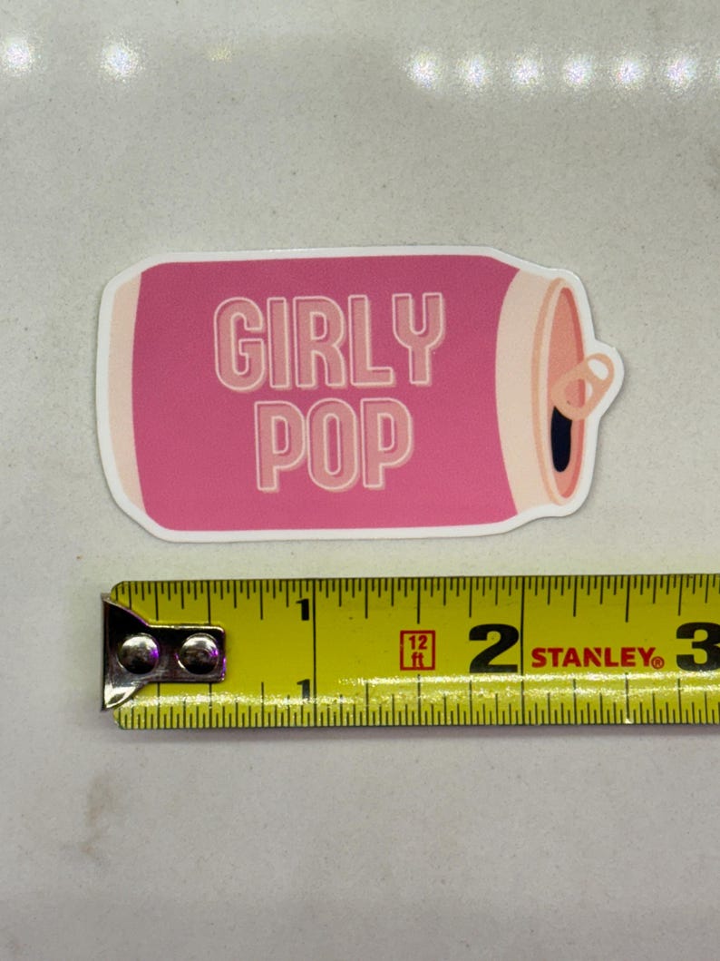 May include: Pink and white sticker of a can with the text "Girly Pop" on it. The sticker is about 2 inches wide.