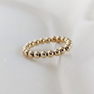Könnte beinhalten: Ein goldener Perlenring mit schlichtem Design. Der Ring besteht aus kleinen, runden Perlen, die gleichmäßig verteilt sind.