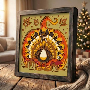 May include: A framed, layered paper art piece featuring a turkey in a pumpkin. The turkey has a top hat and a large, colorful tail. The pumpkin is orange and yellow, with autumn leaves and small pumpkins at the bottom. The frame is dark brown.
