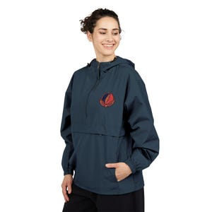 May include: Navy blue anorak jacket with a half-zip closure and a hood. The jacket features a colorful emblem on the chest. The emblem is a stylized design with red, orange, and yellow elements. The jacket has a front pocket and elastic cuffs.