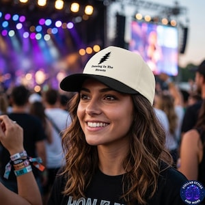 Pode incluir: Boné de beisebol creme e preto com a inscrição "Dancing In The Streets". O boné apresenta um gráfico preto. O boné é usado por uma pessoa em um show ao ar livre.
