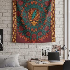 May include: A tapestry with a mandala design featuring a skull with a lightning bolt, surrounded by roses and leaves. The tapestry is predominantly red, orange, and teal, with a gold border. It hangs on a white brick wall.