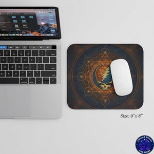 May include: A rectangular mousepad with a colorful design featuring a skull and lightning bolt emblem, surrounded by geometric shapes. The mousepad is 9 inches by 8 inches. A white computer mouse rests on the pad next to a laptop.